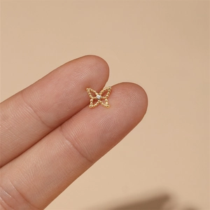 Macro shot of a tiny gold butterfly earring with milgrain edges held between fingers