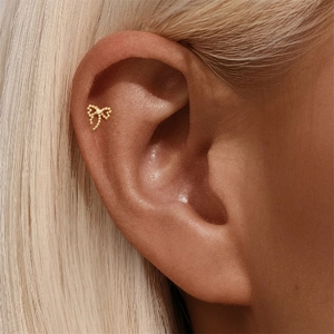 Close-up of a delicate golden bow helix cartilage stud earring in 925 sterling silver