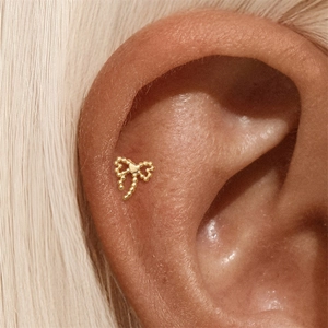 Close-up of a s925 silver golden bow stud earring with heart detail on a woman's ear