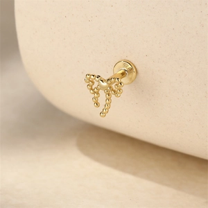 Macro shot of s925 silver golden bow stud earring featuring heart detail on beige stand