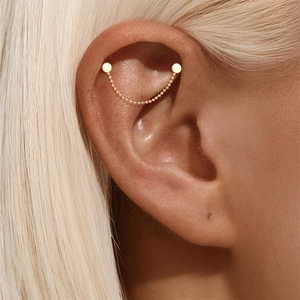 Macro detail of gold helix ear chain featuring bead strand and polished disc studs
