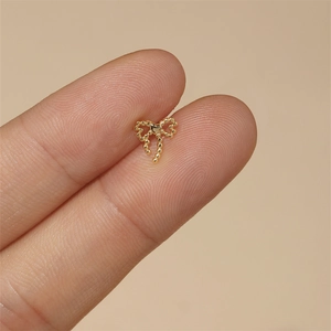 Macro shot of tiny gold beaded bow stud earring with heart detail held on a fingertip