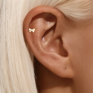 Macro detail of a 14K gold bow cartilage stud earring with a central diamond accent