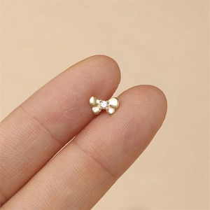 Close-up of a tiny gold S925 silver bow stud earring with a small crystal on a finger