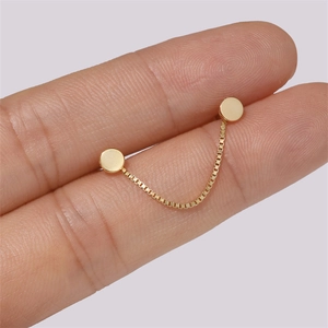 Macro shot of gold double stud earrings with a delicate box chain held between fingers