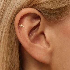 Close-up of golden Saturn planet stud earring with zircon on ear cartilage