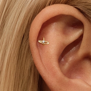 Macro shot of gold planet stud earring with a central zircon worn on the ear cartilage
