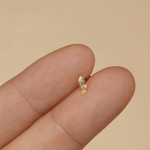 Macro shot of tiny gold leaf stud earrings with a textured glitter finish on a finger