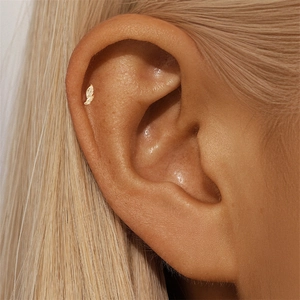 Macro view of a gold leaf-shaped S925 silver helix piercing on a model's ear