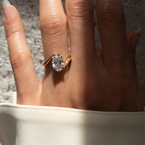 Macro shot of an oval-cut diamond on a wavy gold band worn on a model's hand