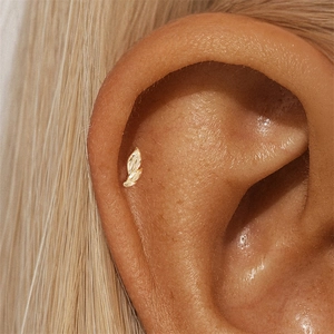 Close-up of a golden leaf-shaped cartilage stud earring worn on the earlobe
