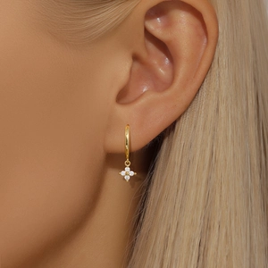 Close-up of elegant gold hoop earrings with white four-petal flower zircon pendant