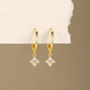 Detail of gold hoop earrings with star-shaped pendants and white crystal insets