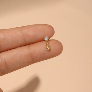 Makroaufnahme von goldenem Tropfenohrring mit Zirkon-Stecker zwischen den Fingern