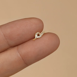 Macro view of a gold S-shaped ear stud with sparkling cubic zirconia on fingertips