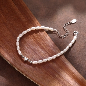 Vista detallada de pulsera de perlas de arroz con colgante de corazón plateado sobre madera