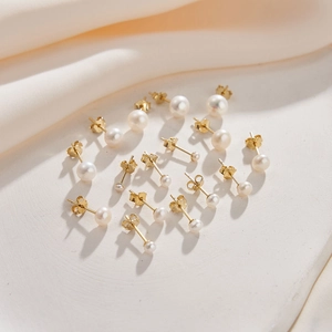 Elegant gold-plated pearl stud earrings set in various sizes on beige silk fabric