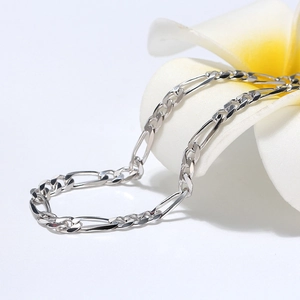 Detailed macro shot of a 5mm S925 sterling silver Figaro chain with a white floral prop