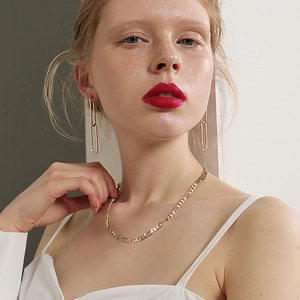 Vue détaillée d'un collier chaîne Figaro doré et de boucles d'oreilles sur un modèle
