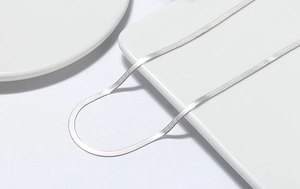 Macro shot of polished silver snake chain necklace on minimalist geometric display