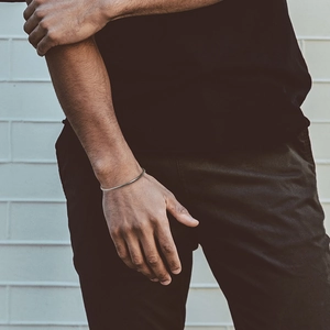 Close-up of minimalist silver snake chain bracelet worn on wrist against a white wall