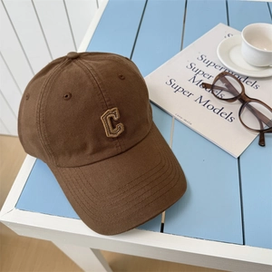 Casquette de baseball marron avec logo C brodé sur une table rayée avec accessoires