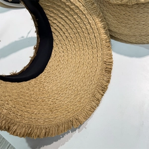 Detailed close-up of natural straw sun hat featuring fringe edges and black sweatband