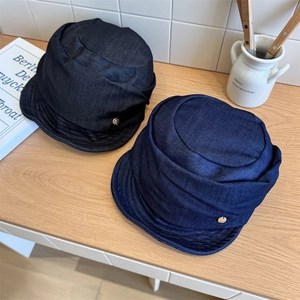 Gorras de marinero vintage en denim negro y azul con logo dorado sobre mesa de madera
