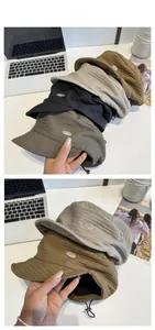 Detail of pleated textured bucket hat featuring an adjustable drawstring and metal logo plate