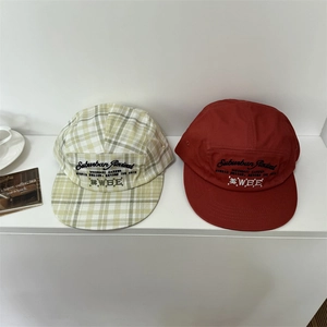 Flat lay of retro plaid and solid red five-panel hats with Suburban Revival embroidery