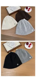 Detailed flat lay of knit beanies in ivory and brown with metal logo on wooden surface