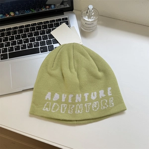 Light green knit beanie with Adventure embroidery on a clean desk with accessories