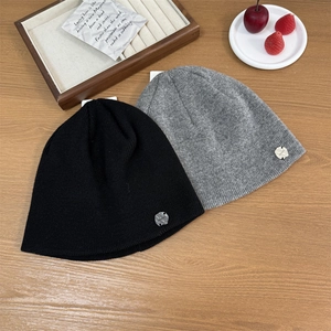 Black and grey knitted beanies with round metal emblems on a wooden surface