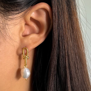 Close-up of a U-shaped gold link earring with a natural baroque pearl worn by a model