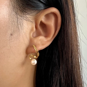 Macro side view of a model wearing a spiral gold earring with a white baroque pearl
