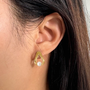 Close-up of geometric gold hollow triangle earrings with white baroque pearls on ear