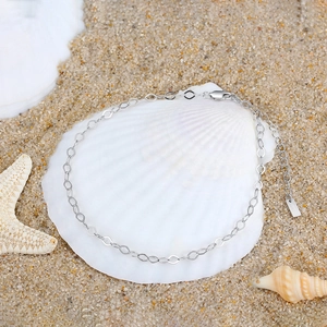 Minimalist S925 sterling silver rhombic link anklet displayed on a seashell and beach sand