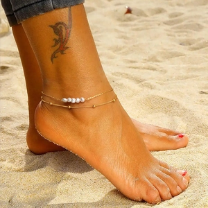 Detail of a gold S925 silver double-layered anklet with pearls on a beach setting