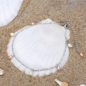 Detail of silver S925 anklet with pearls on a sea shell background at the beach