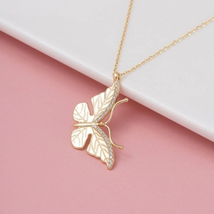 Elegant gold butterfly necklace with crystal wings on a minimalist white ceramic tray