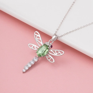 Elegant hollow dragonfly necklace with green crystal and silver chain on pink background