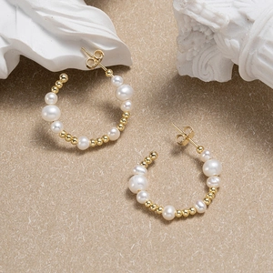 Baroque pearl C-shape hoop earrings with gold-plated metal beads on a textured surface