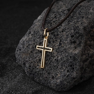 Dettaglio di un ciondolo a croce dorata traforata su una collana in corda di cuoio