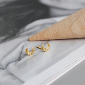 Vue macro de boucles d'oreilles croissants dorés sertis de zircons sur tissu