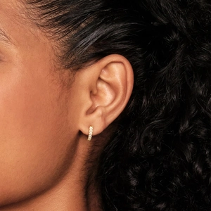 Close-up of a gold huggie earring with shimmering pavé zircon stones on an earlobe