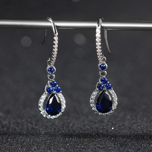 Close-up of pear-cut blue sapphire drop earrings with silver prongs on black background