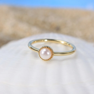 Bague dorée avec perle baroque et base ciselée sur un coquillage face à l'océan