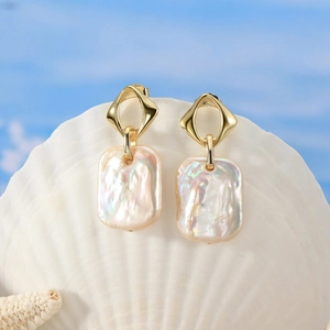 Détail de boucles d'oreilles pendantes en perles baroques posées sur un coquillage