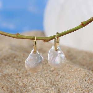 Gold baroque pearl earrings hanging on a green branch with beach background