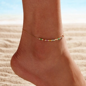 Detail of gold beaded anklet with colorful charms on a model at a sunny summer beach